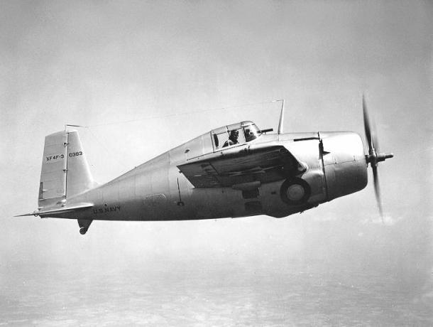 Grumman XF4F-3 Wildcat עף משמאל לימין, גימור אלומיניום מכסף, טייס משקיף החוצה.